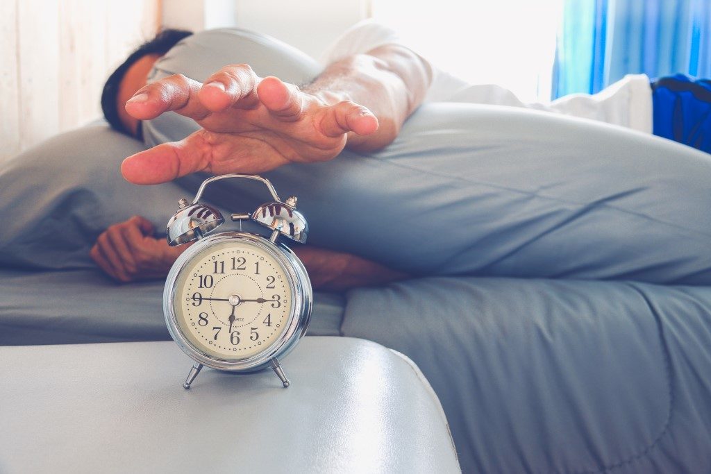 picture of man in bed trying to press alarm clock